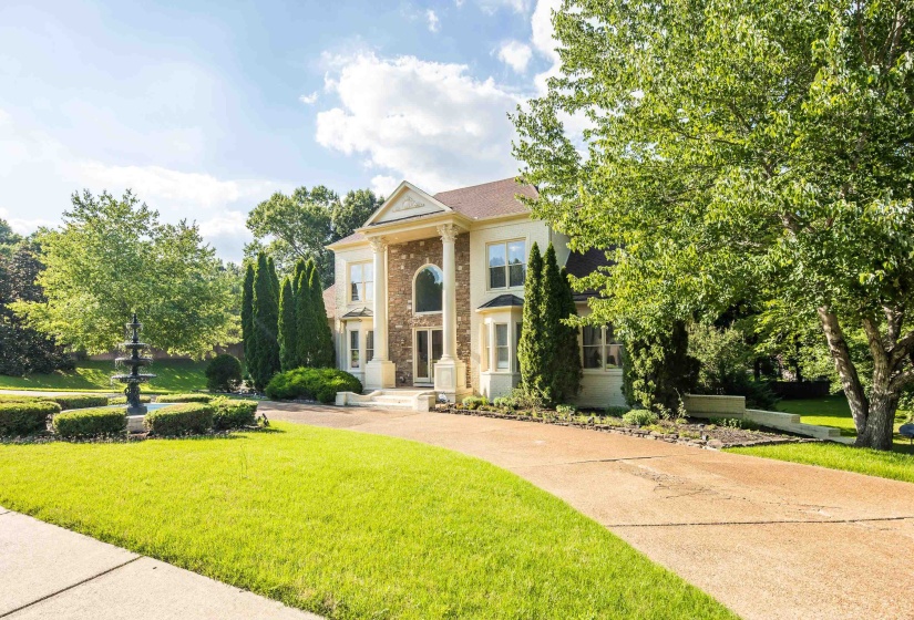 Stately multi-story residence featuring a grand portico with columns, arched entry, and bay window