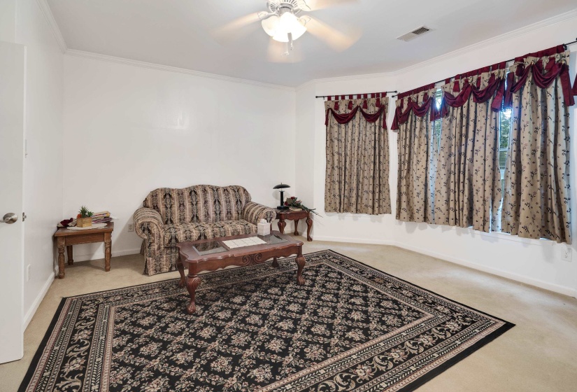 Carpeted interior space featuring a bay window, ceiling fan, and white painted walls