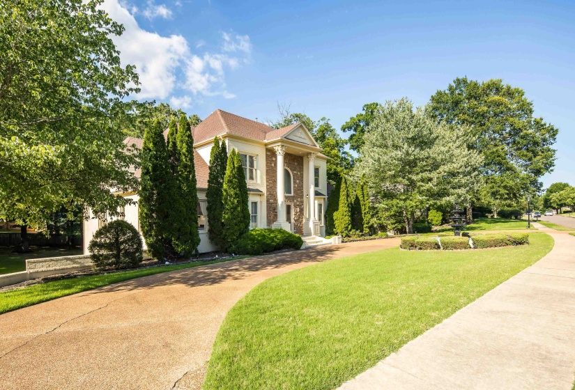 Stately stucco exterior with prominent columns, a terracotta-toned roof, and a mature treed setting