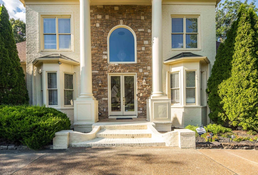 Stately brick and stone exterior with a prominent arched window and double glass-paneled entry doors