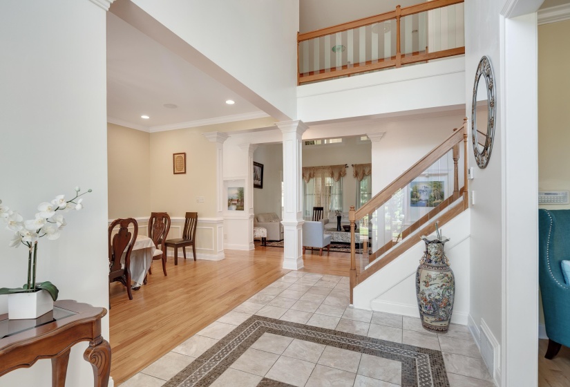 Two-story foyer featuring tile flooring with decorative inlay, hardwood flooring, a staircase with wood newel posts and glass balusters, and a second-story overlook with wood railing