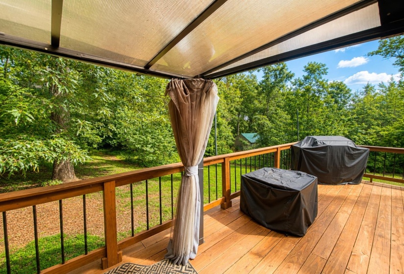 Expansive wood deck with a translucent overhead cover, featuring a sturdy wood railing with black spindles