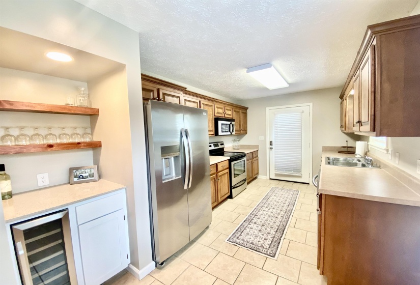 Kitchen featuring stainless steel appliances, wood cabinetry, and a dedicated beverage station with floating shelves and an under-counter refrigerator