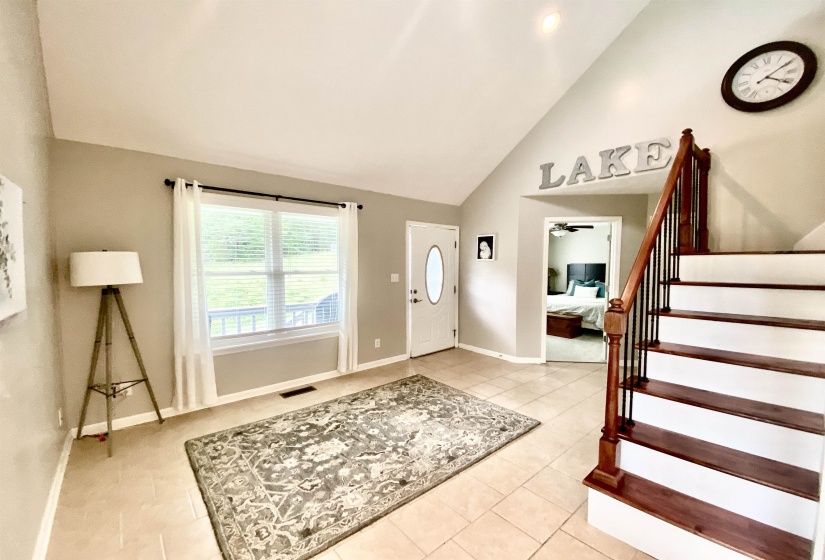 Tiled entryway with vaulted ceiling, wood-finish staircase with wrought iron balusters, and a front entry door with an oval glass insert