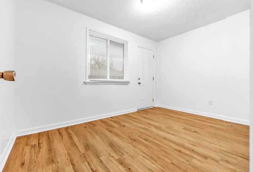 Room featuring wood-finish flooring, white baseboards, and a white interior door
