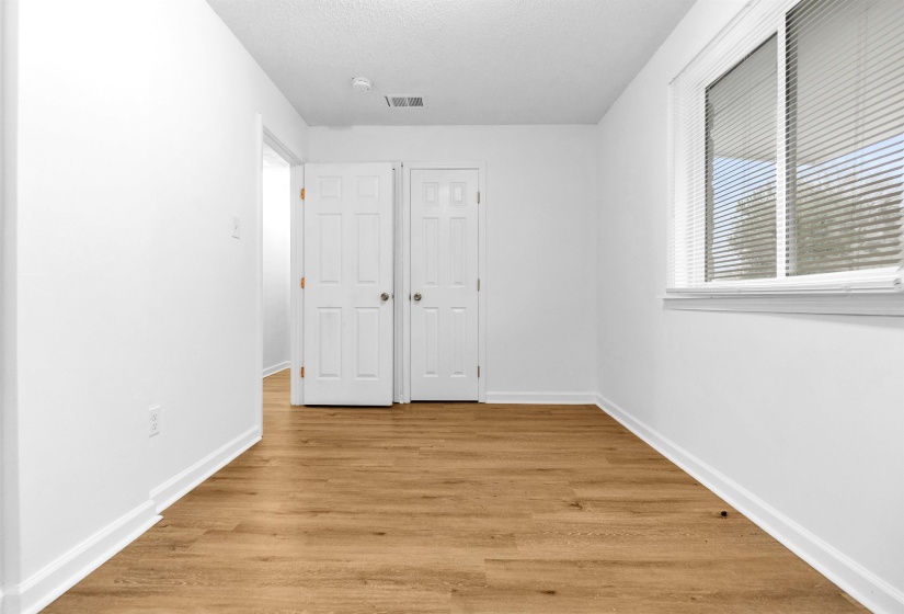 Spacious room with wood-finish flooring, white walls, and a large window featuring blinds
