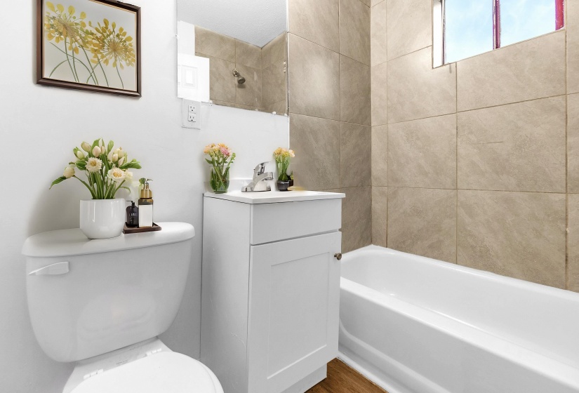 Bathroom featuring a white vanity with a chrome faucet, toilet, and a bathtub with large format tile surround