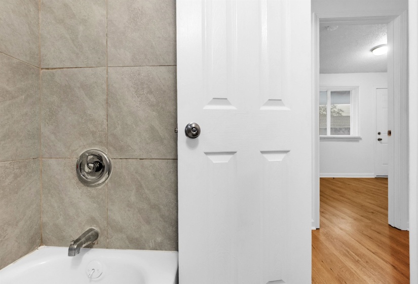Bathroom featuring a white bathtub with chrome fixtures and light-toned tile surround