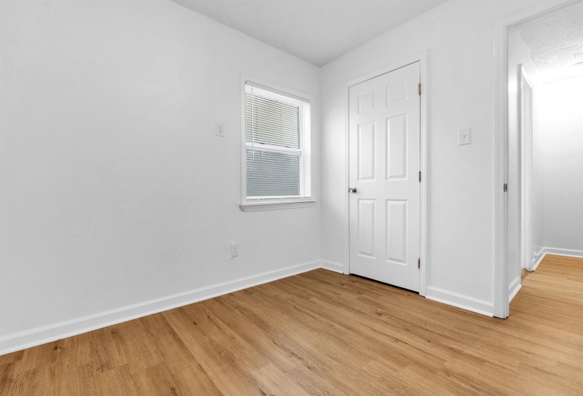 Room featuring wood-finish flooring, white baseboards, and a single window with horizontal blinds