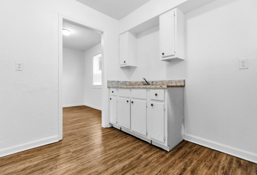 Compact kitchen area featuring white cabinetry, a single basin sink with a chrome faucet, and a light-toned countertop