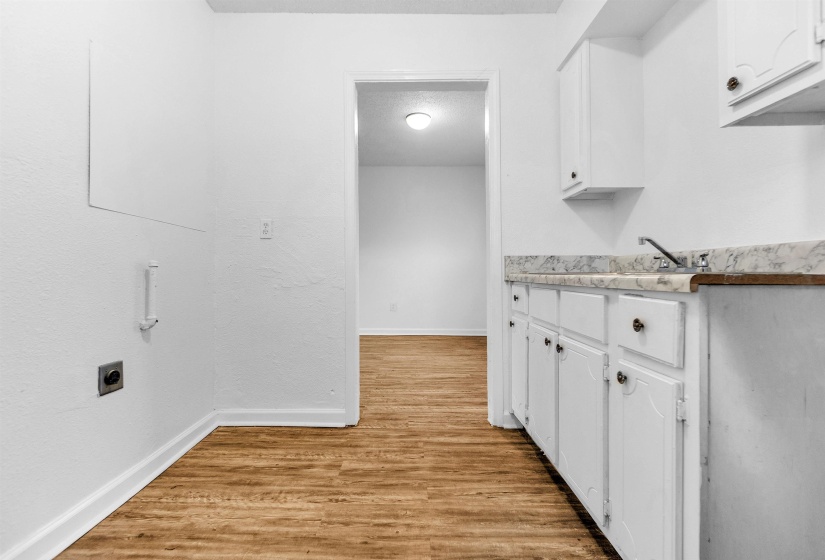 Utility area featuring wood-finish flooring, white cabinetry with dark hardware, a sink with a chrome faucet, and appliance hookups