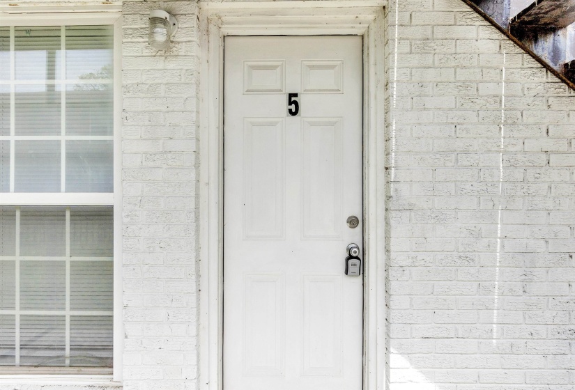 White painted brick exterior with a panel door, featuring a traditional door handle and a unit number