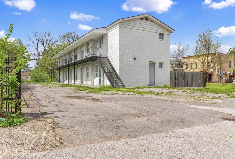 Two-story apartment building with white brick facade, individual balcony access for upper units, and a ground-level patio for lower units