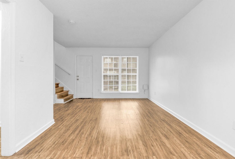 Spacious living area featuring wood-finish flooring, white baseboards, and a multi-pane window