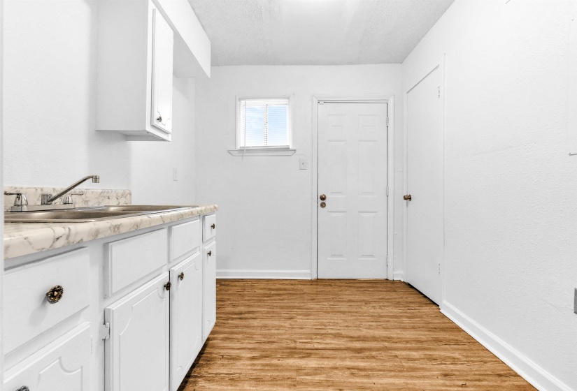 Kitchen area featuring white cabinetry, a single basin sink with a chrome faucet, and wood-finish flooring