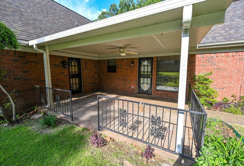 Covered back patio with brick flooring and ceiling fan.