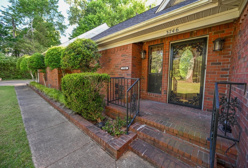 Brick exterior with a brick-paved front entry, featuring a decorative glass storm door, side light window, and black wrought iron railings.