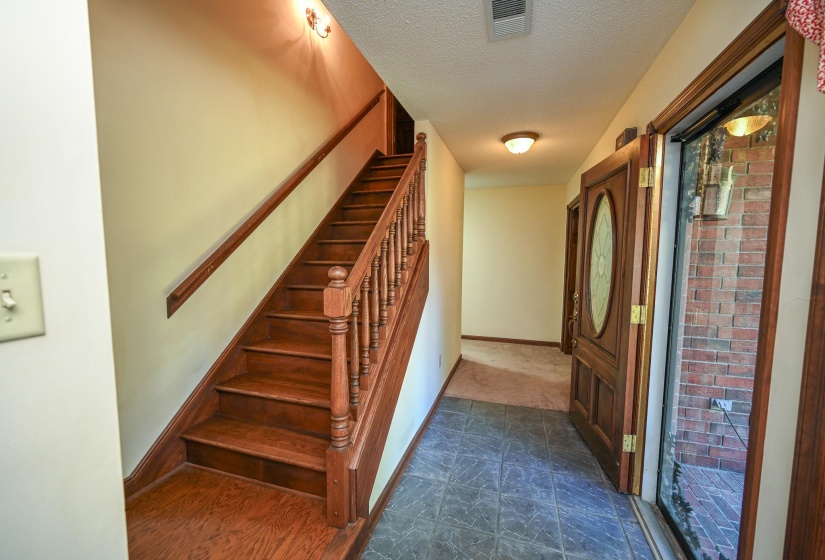 Entryway featuring a wood-finish staircase with baluster railing, tile flooring, and a decorative wood-panel front door with an oval glass insert.
