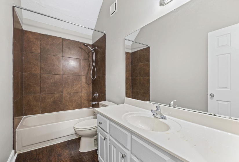 Bathroom featuring a white vanity with an integrated sink, a large wall-mounted mirror, and a combination tub and shower with brown tile surround