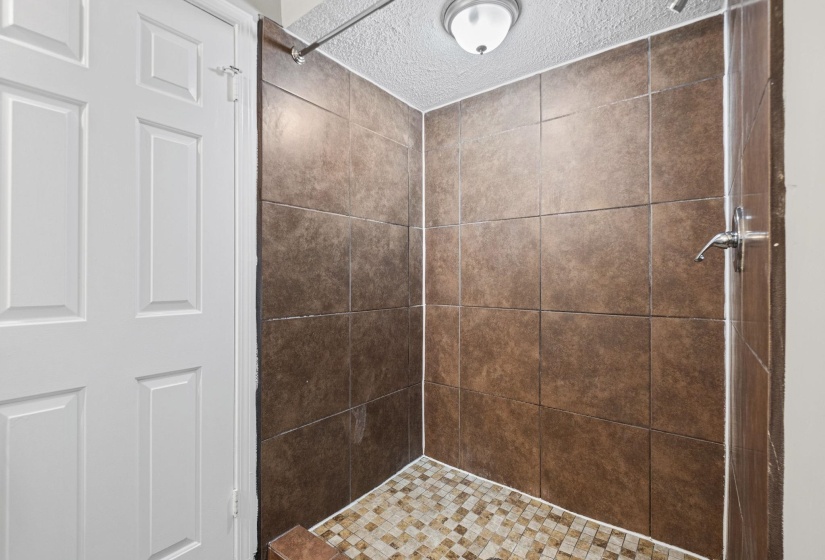 Shower enclosure with brown square wall tiles and mosaic tile flooring