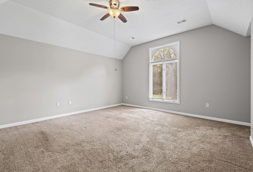 Spacious interior room featuring a vaulted ceiling with a ceiling fan, a large arch-top window, light grey walls, and plush carpet flooring