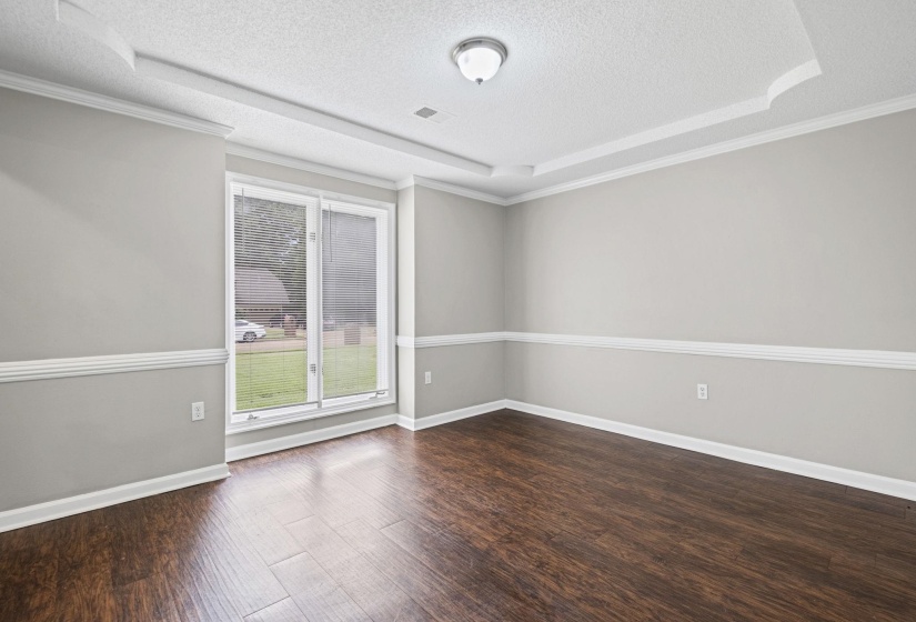 Room featuring wood-finish flooring, light gray walls with chair rail molding, and a tray ceiling with crown molding