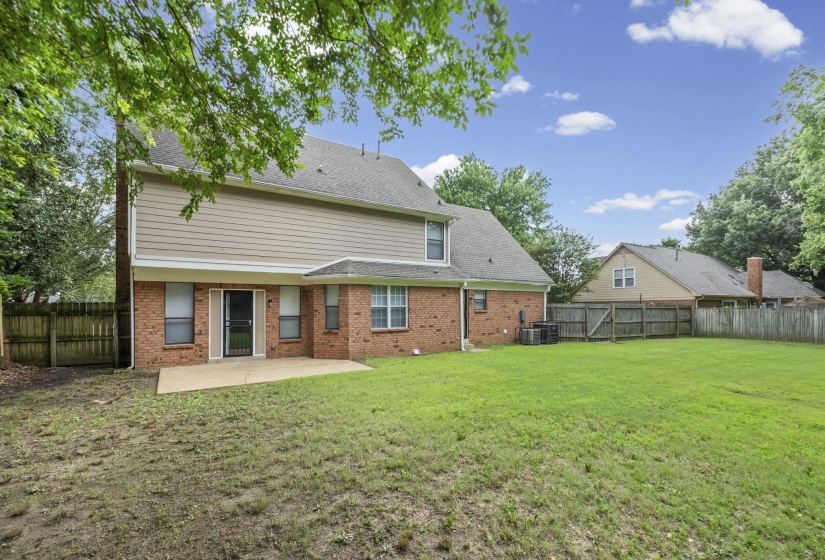 Spacious backyard featuring a brick and siding exterior, a concrete patio, and a wood privacy fence