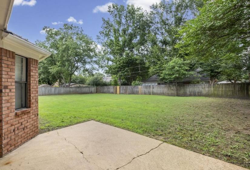 Spacious backyard featuring a concrete patio, expansive green lawn, and wood privacy fencing