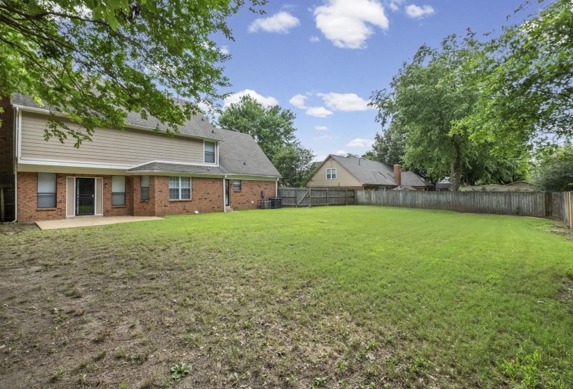 Expansive backyard featuring a large grass area, wood privacy fence, and mature trees