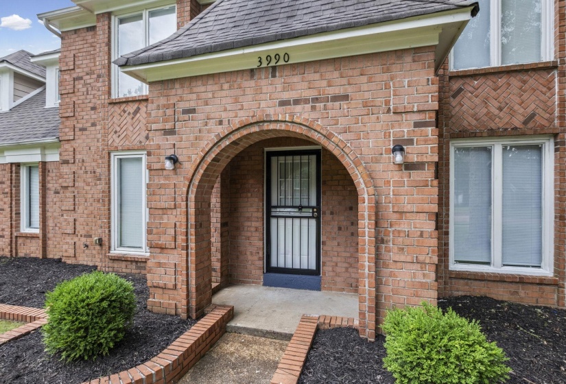 Brick exterior with arched entryway, security screen door, and exterior sconce lighting