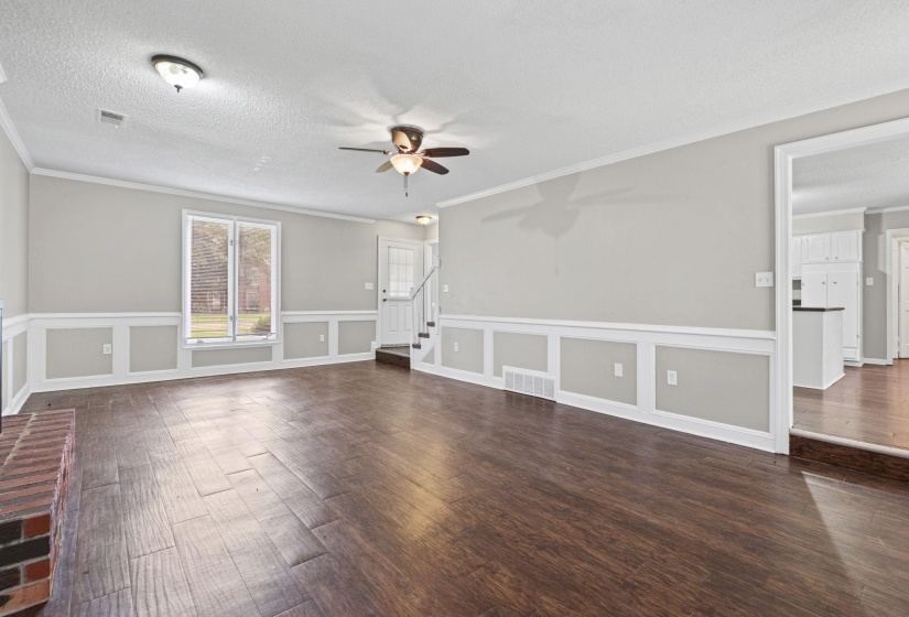Spacious living area featuring wood-finish flooring, a brick fireplace, wainscoting, and large windows