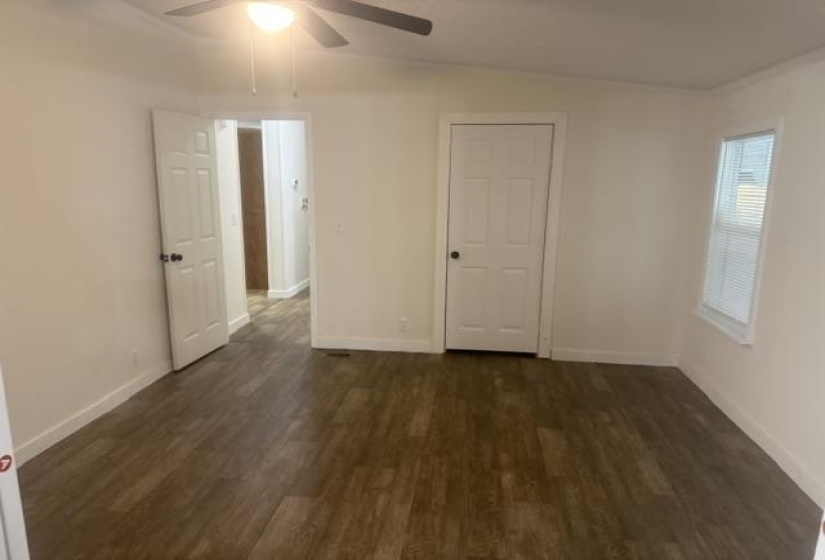Room featuring wood-finish flooring, white paneled doors, and a ceiling fan with integrated lighting