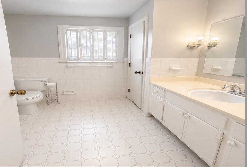 Bathroom featuring octagon-patterned floor tiles, white subway tile wainscoting, white vanity with integrated sink, chrome faucet, and plantation shutters