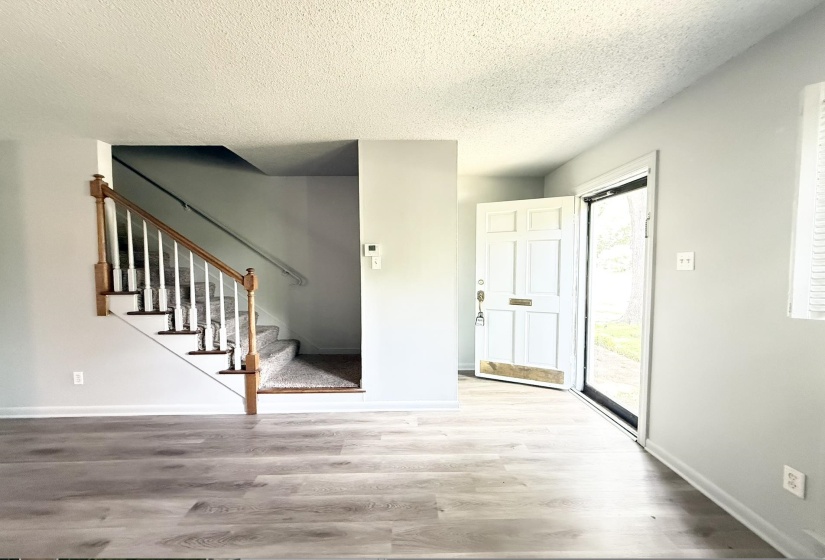 Entryway featuring wood-finish flooring, a paneled front door, white trim, and a staircase with wood handrails and carpeted treads