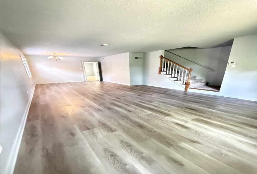 Spacious living area featuring wood-finish flooring, light grey wall tones, and a chandelier-style ceiling fixture