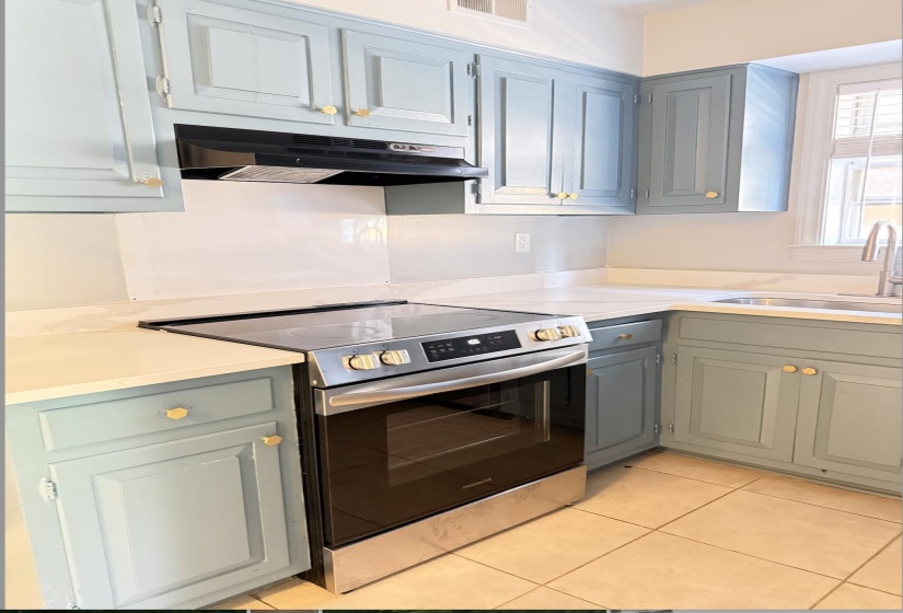 Kitchen featuring light blue cabinetry with gold-tone hardware, white countertops, a stainless steel range, and a coordinating range hood