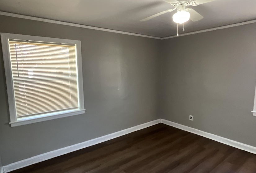 Empty room with dark wood finished floors, crown molding, baseboards, and ceiling fan