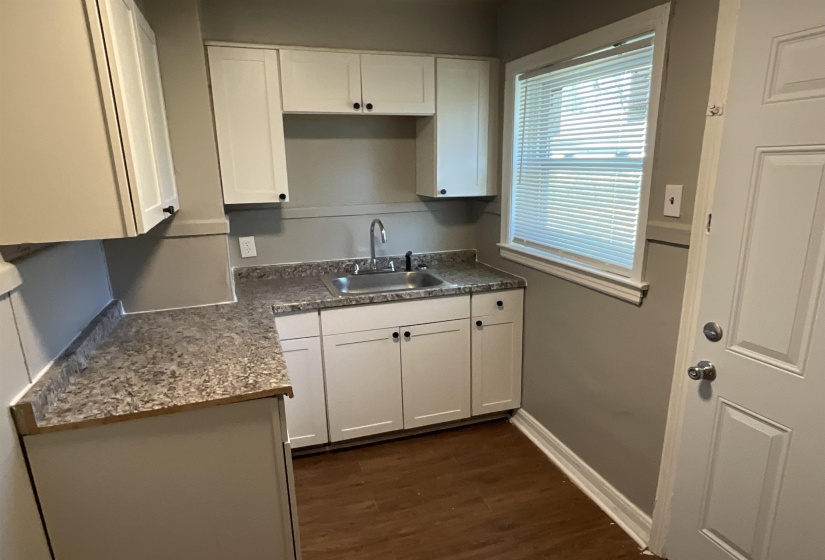 Kitchen featuring baseboards, dark countertops, dark wood-type flooring, white cabinetry, and a sink