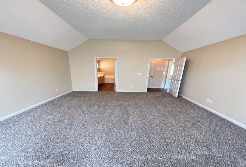Unfurnished bedroom featuring lofted ceiling, dark carpet, a textured ceiling, and connected bathroom