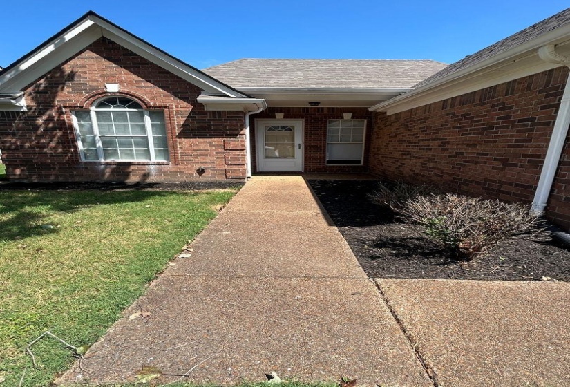 Property entrance featuring brick siding, a lawn, and a shingled roof