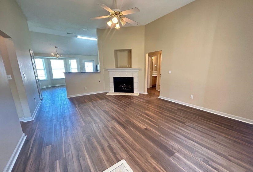 Unfurnished living room with dark wood finished floors, a ceiling fan, a chandelier, a fireplace, and high vaulted ceiling