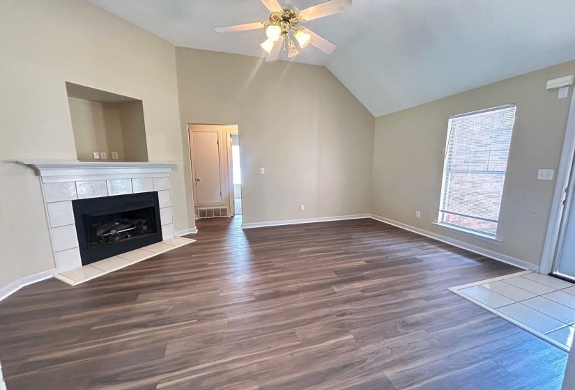 Unfurnished living room with dark wood-type flooring, a ceiling fan, a tile fireplace, and high vaulted ceiling