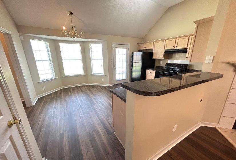 Kitchen with dark wood-style floors, vaulted ceiling, light brown cabinets, black appliances, and a chandelier