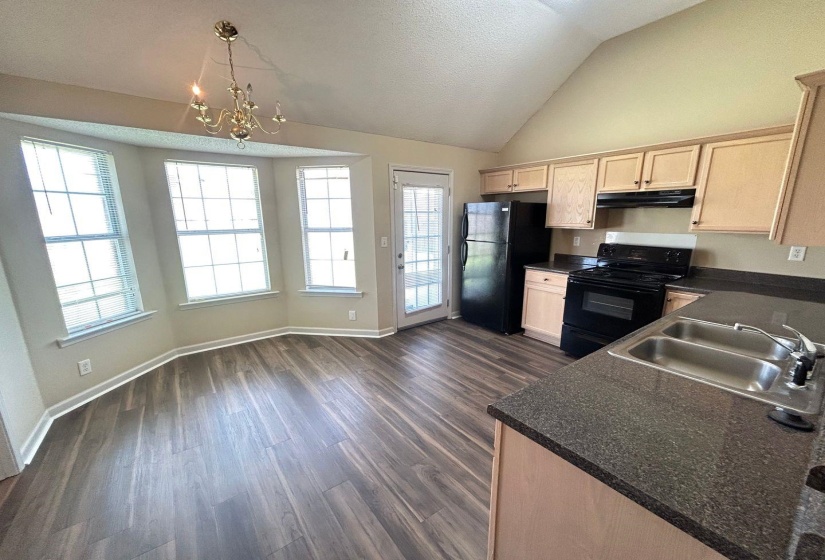 Kitchen with black appliances, light brown cabinets, dark wood finished floors, a chandelier, and lofted ceiling