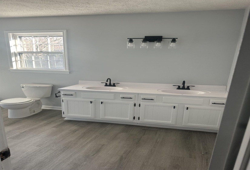 Bathroom featuring double vanity, a textured ceiling, and light wood-style floors