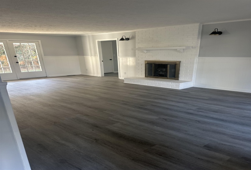 Unfurnished living room with wainscoting, dark wood finished floors, a brick fireplace, and a textured ceiling