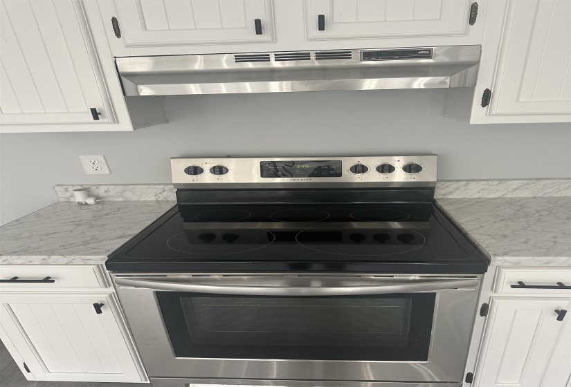 Kitchen with under cabinet range hood, stainless steel range with electric cooktop, and white cabinetry