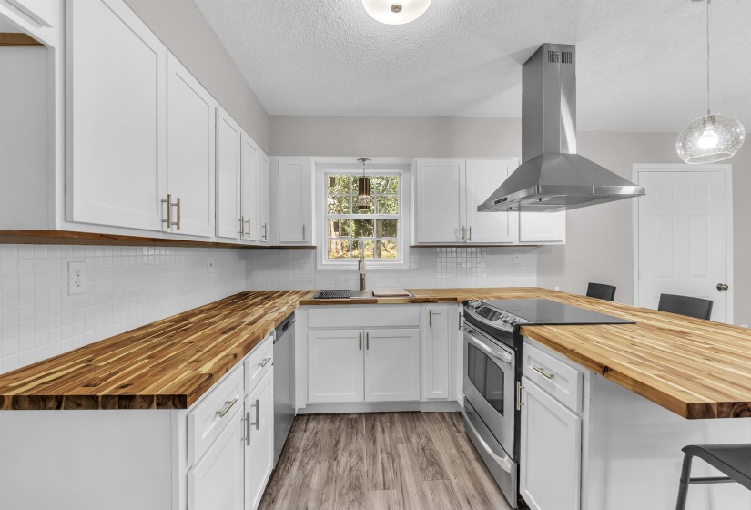 Kitchen featuring butcher block countertops, a kitchen bar, stainless steel appliances, island exhaust hood, and a textured ceiling