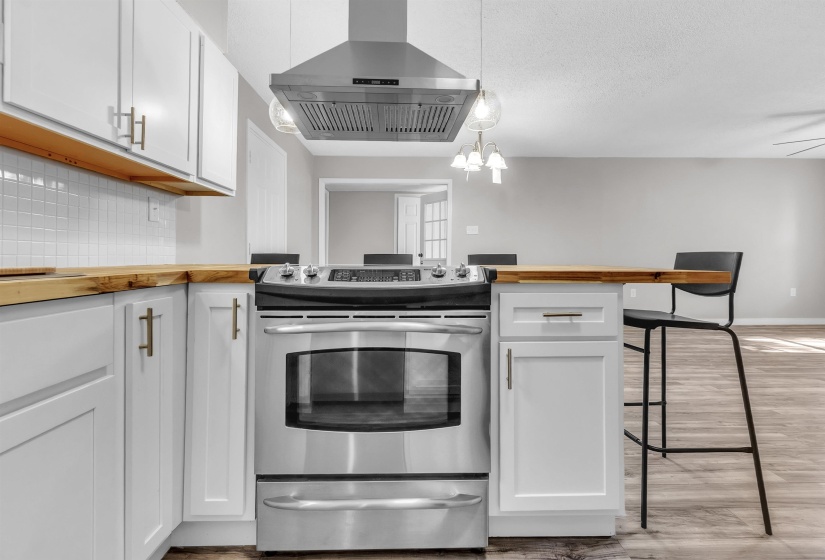 Kitchen featuring wood counters, white cabinets, stainless steel electric range oven, and a breakfast bar