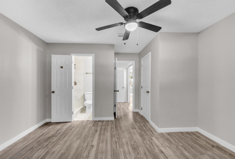 Unfurnished bedroom featuring light wood-style floors, ceiling fan, ensuite bathroom, and a textured ceiling